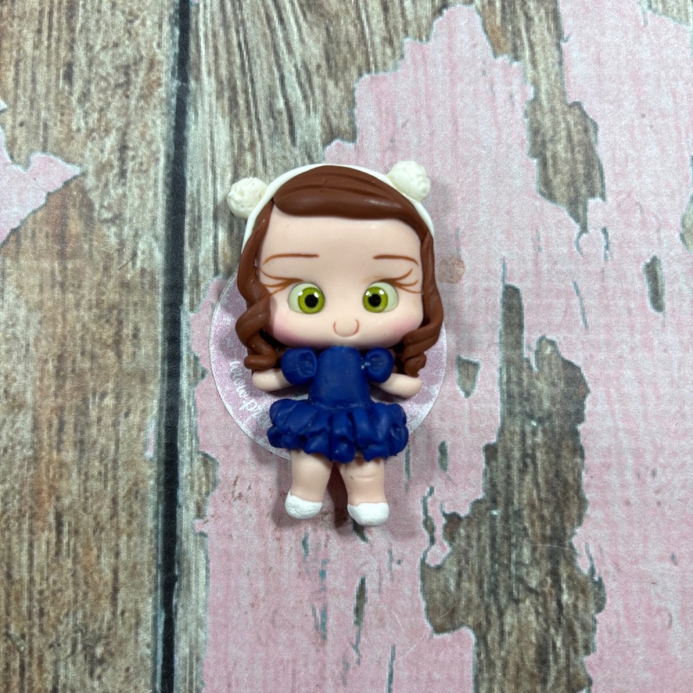 Little girl, blue pom-pom dress, white headband, brown hair, green eyes