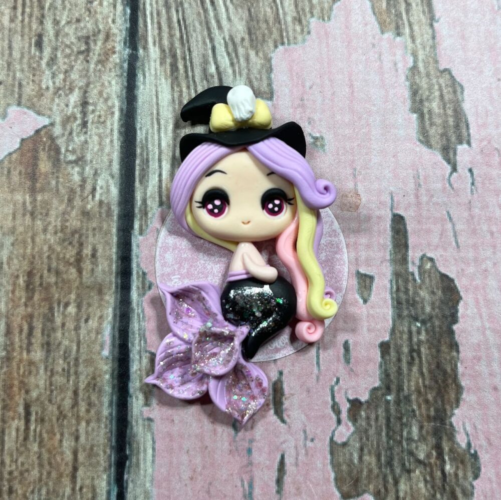 Little girl with a black mermaid tail and purple fins, a mix of purple yellow and pink hair and a black witches hat