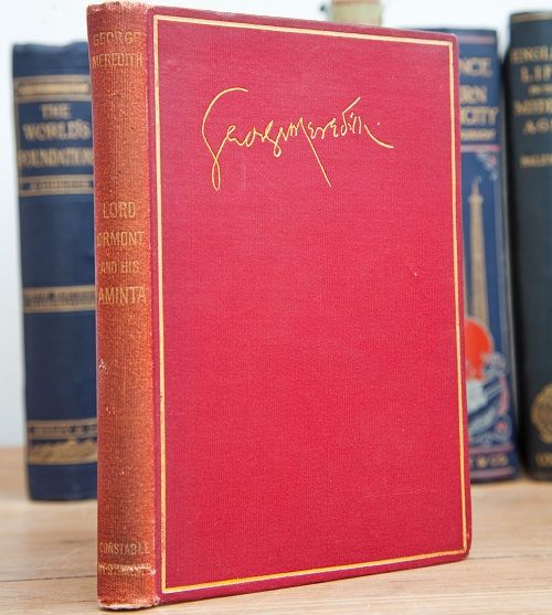 A red vintage book with a gilt embossed signature on the front.