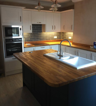 Photo of a kitchen island, with navy cupboards and wooden worktop, and enamel sink