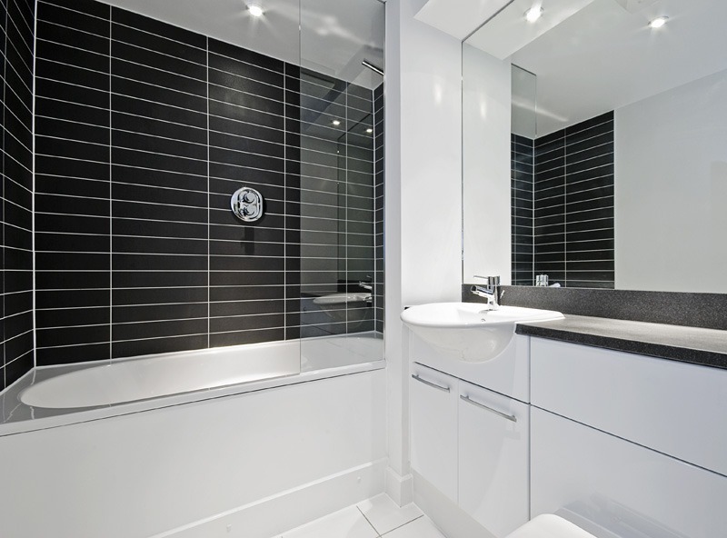 Photo of a modern, sleek, white bathroom suite with black wall tiles
