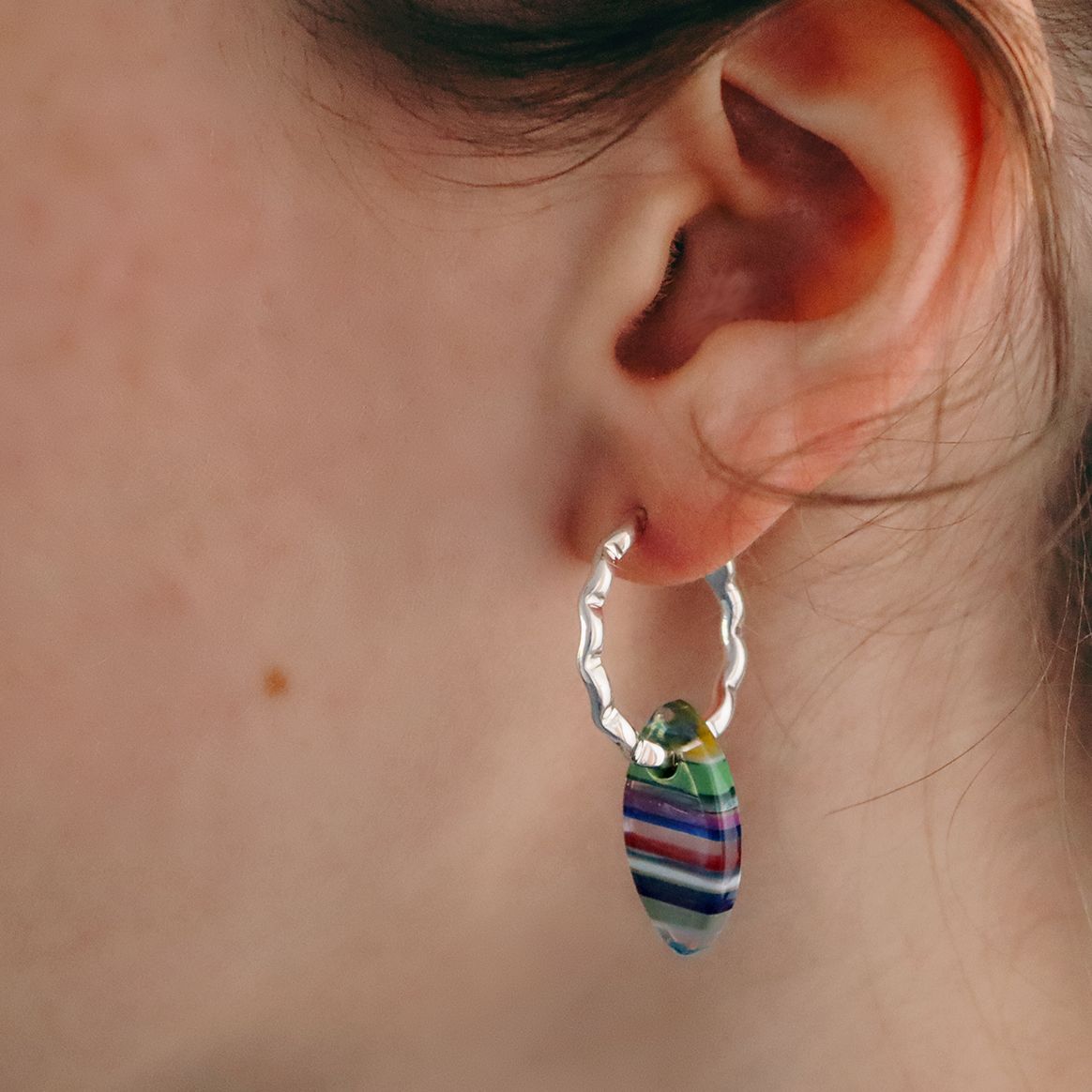 Women wearing a wavy silver hoop with striped Surfite charm hanging off the hoop