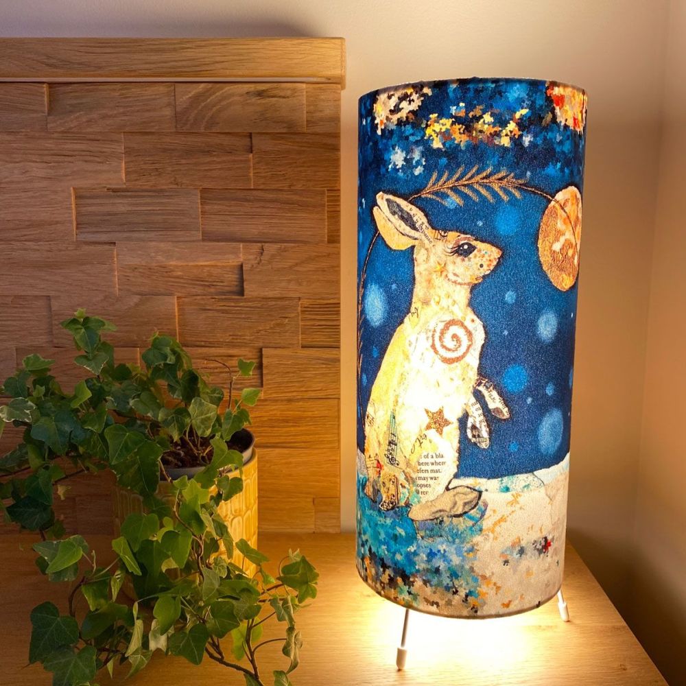 Luna Hare Cylinder Table Lamp at night on table with ivy