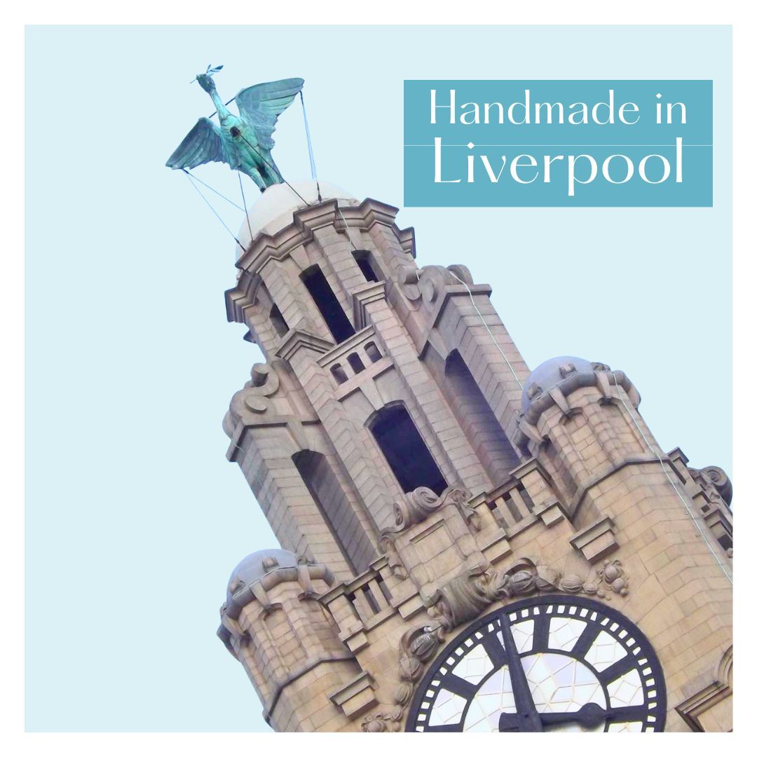 One of the two clock towers of the Liver Building in Liverpool with a Liver Bird on the dome  at the top. There is a teal block to the right of the picture with the words Handmade in Liverpool