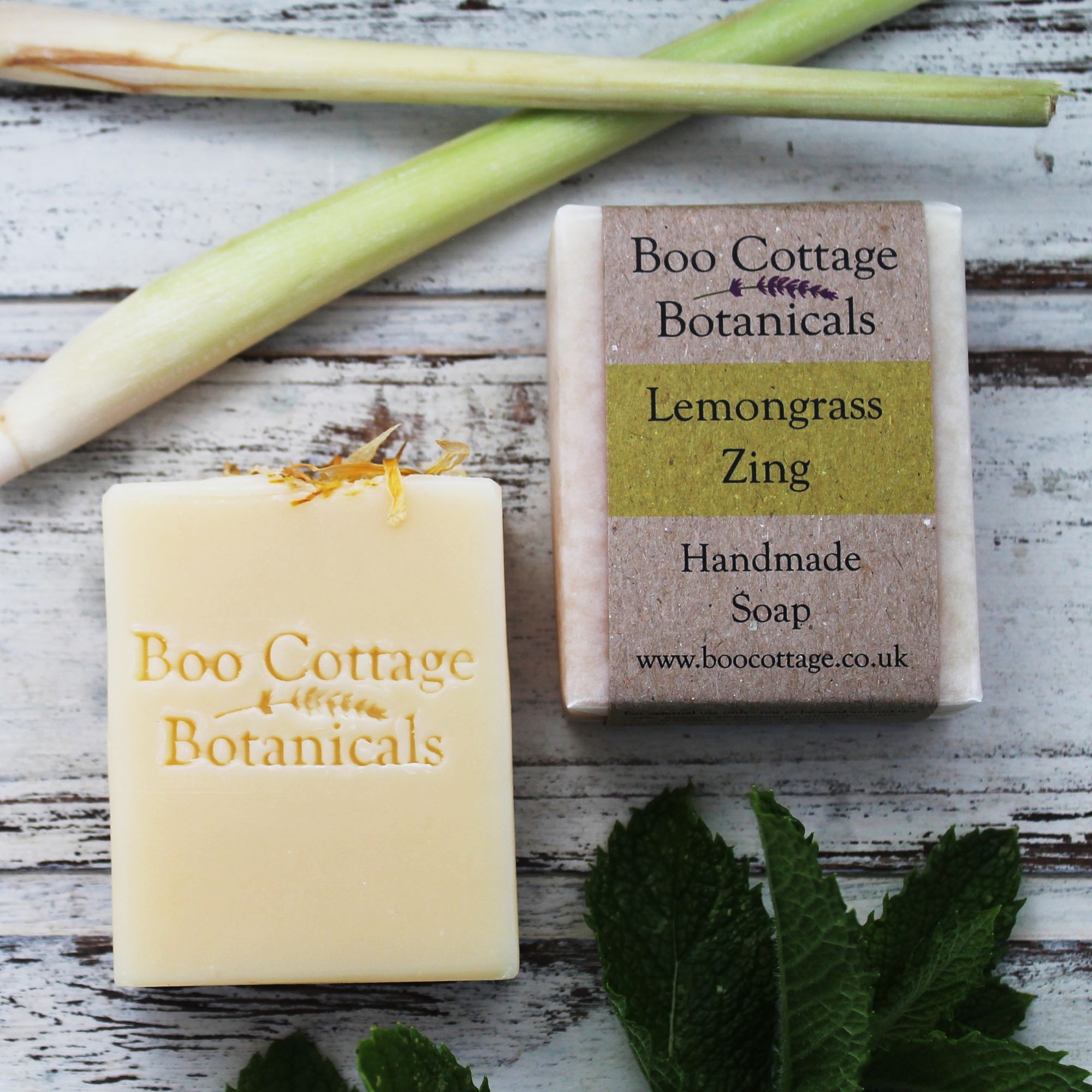 Yellow unwrapped bar of soap next to wrapped bar with lemongrass above