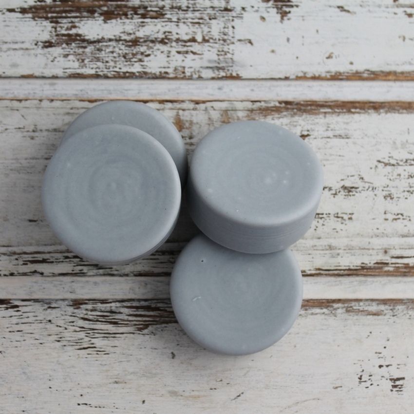 Four light grey tea and charcoal conditioner bars on a white wooden tray.
