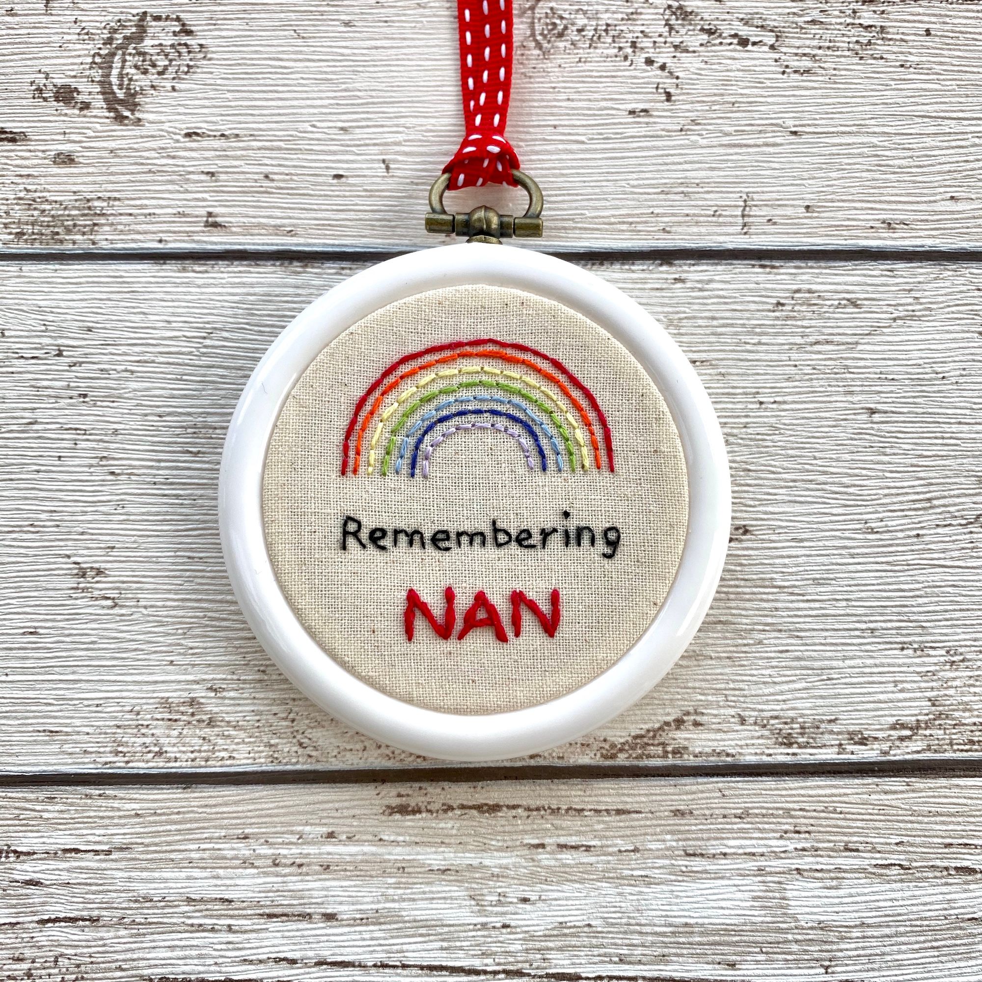 A white hoop with a stitched rainbow over the stitched words Remembering Nan.  Shown on a wooden surface.