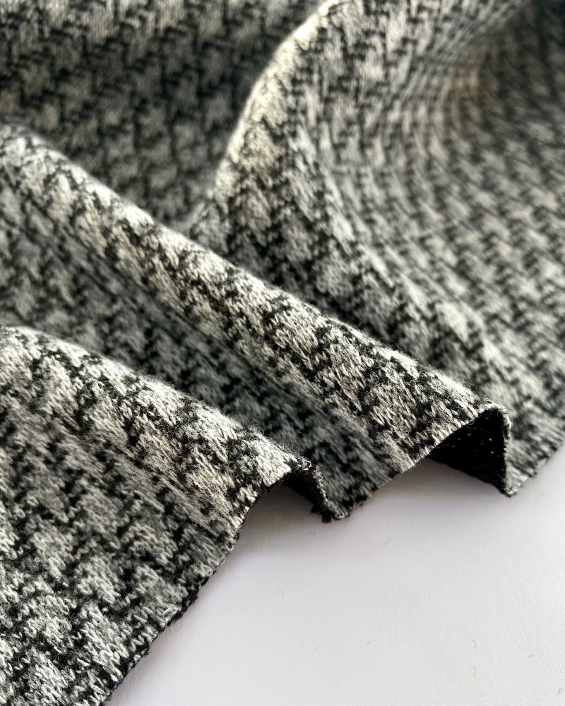 Black and grey textured woolly fabric laid on a white background and showing the edges in waves.  Photo by Just Sew Helen