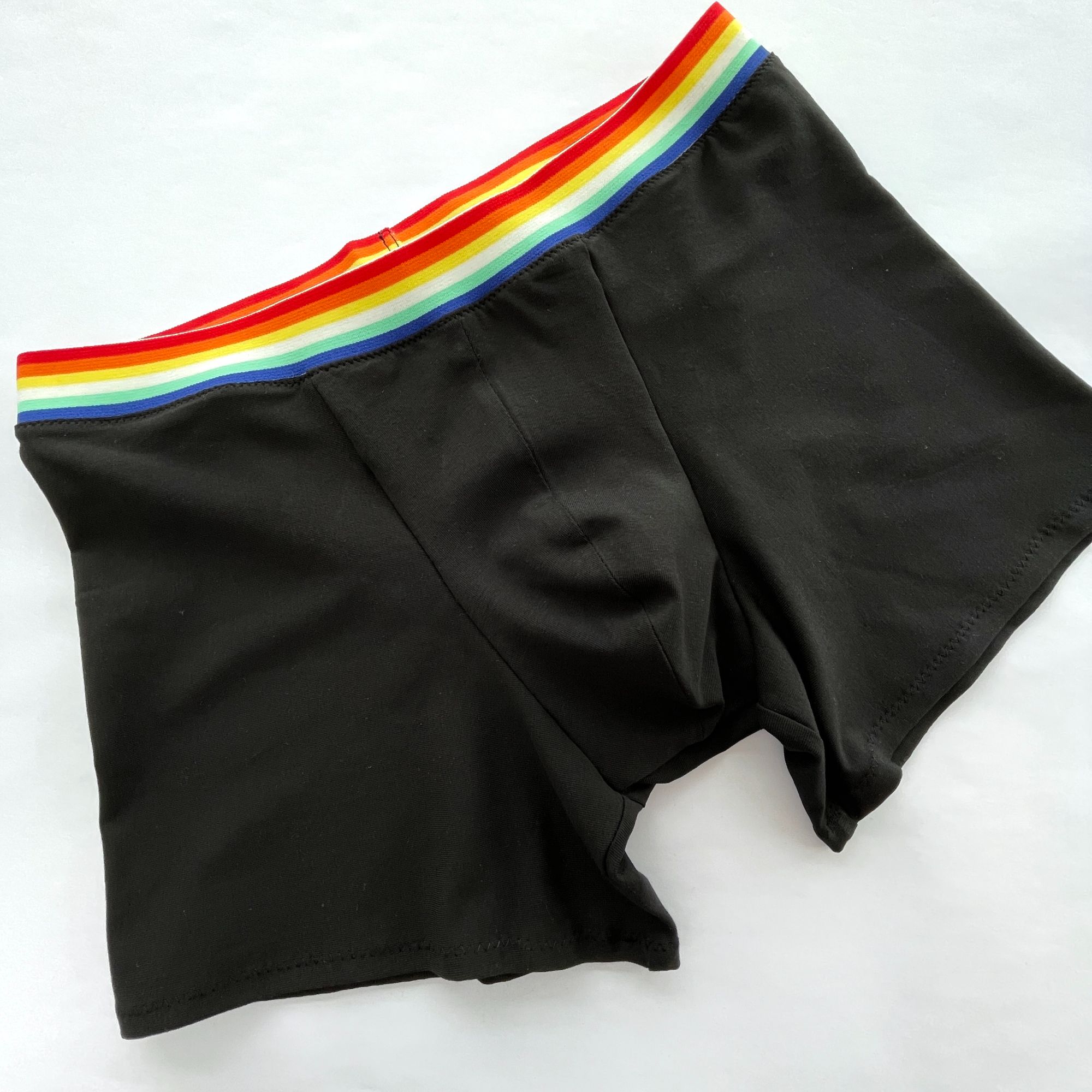 A pair of men's black boxer shorts with rainbow coloured waist elastic. Laid on a white background.