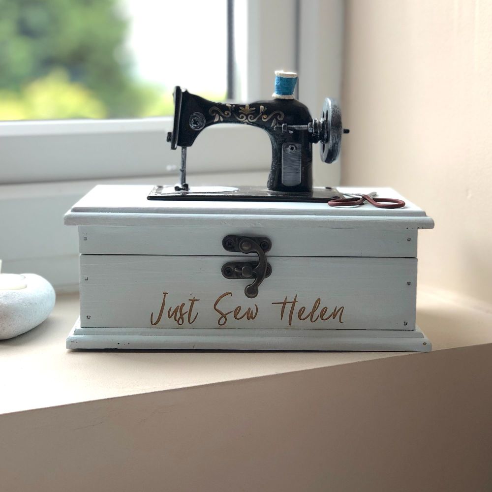 A pale blue wooden box with a front catch and a model sewing machine on the top.  The words Just Sew Helen are burnt onto the front of the box