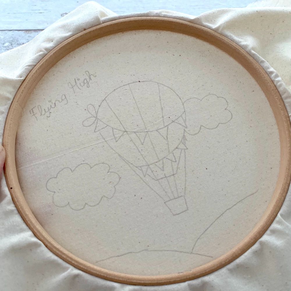 A wooden embroidery hoop and natural cotton fabric inside with a hot air balloon drawn on in pencil.