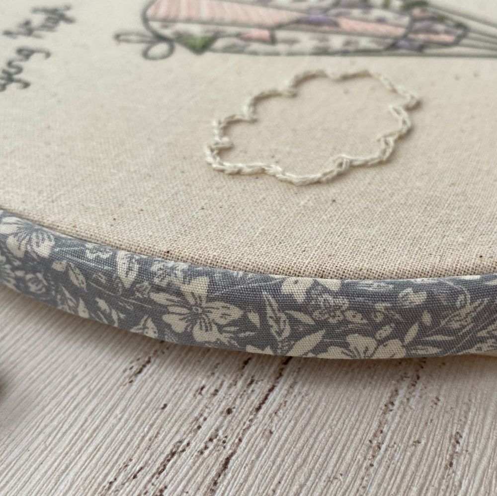 The edge of an embroidery hoop covered with grey floral fabric