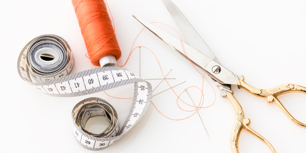 Sewing Kit of scissors, orange thread, tape measure, needle and pins on a white background