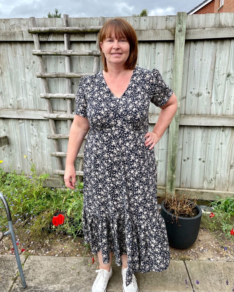 A lady standing in a garden in front of a fence wearing a navy floral viscose dress made using pattern Simplicity 8875