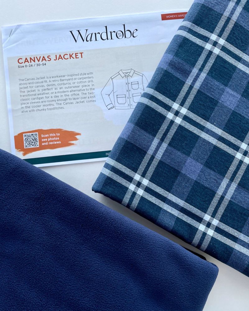 Folded blue check fabric next to navy blue fleece and a jacket sewing pattern