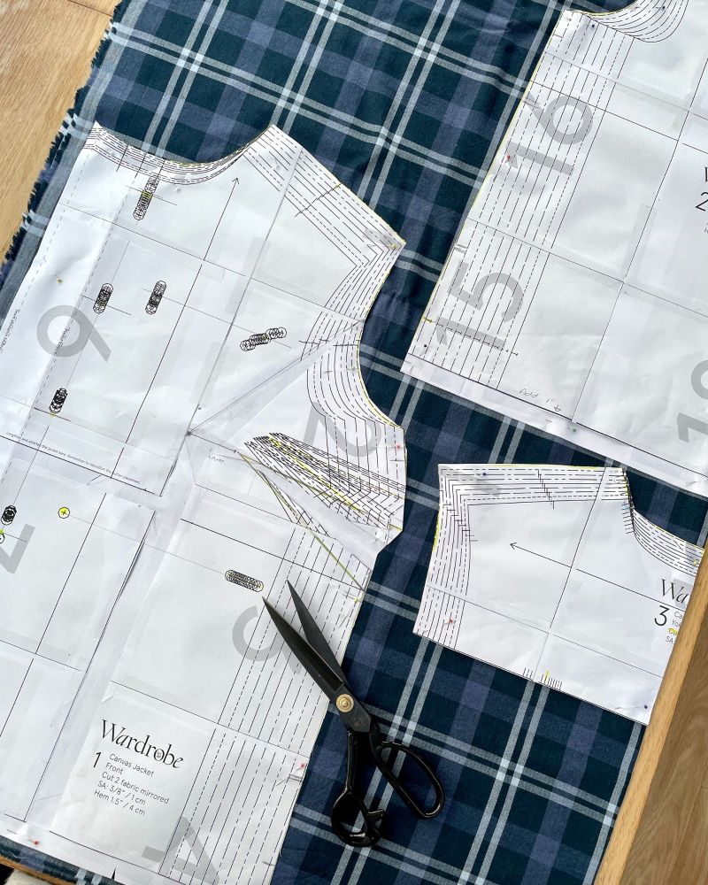 Sewing pattern pieces pinned on to blue checked fabric with a pair of black dressmaking scissors
