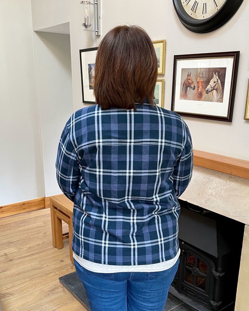 A lady standing in front of a fire place showing the back of a blue checked jacket