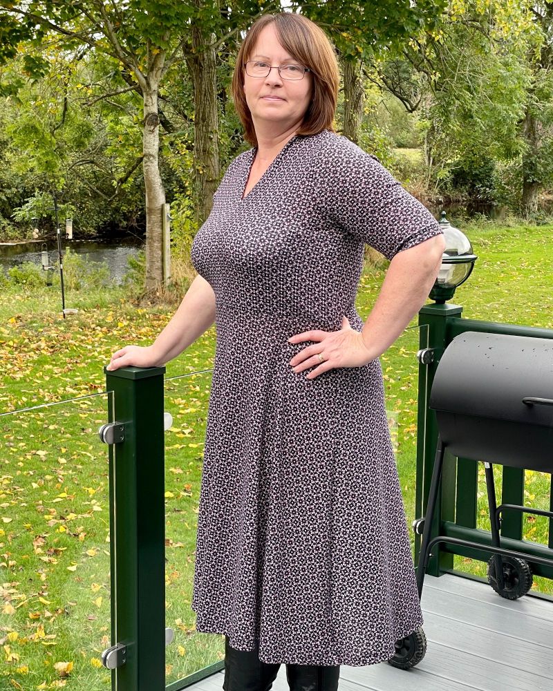 A lady standing in the countryside wearing a black and pink geometric knee length dress