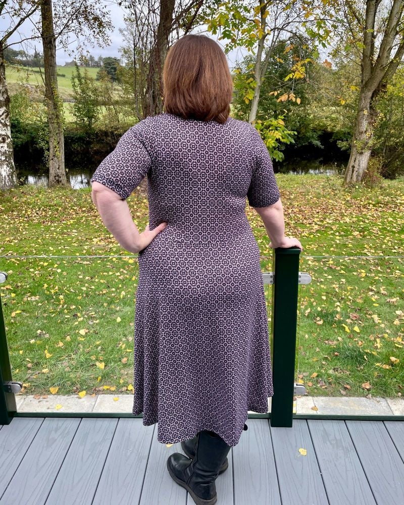 A lady standing on decking with her back to the camera wearing a pink and black knit dressOlympia dress back