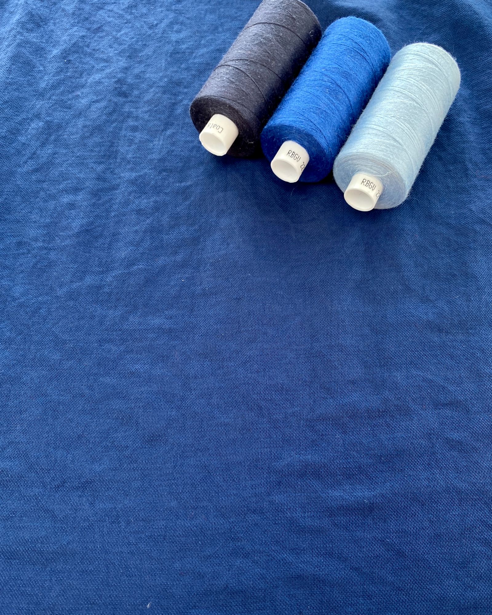 Navy fabric lain flat with three cotton reels in different shades of blue