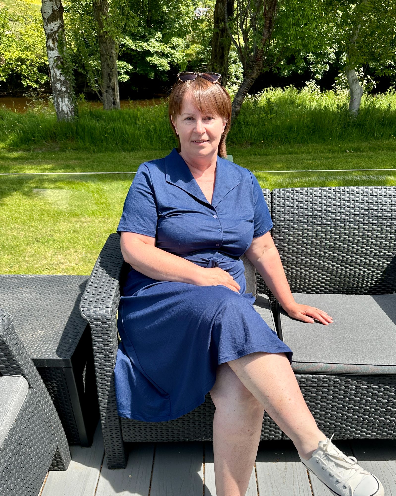 A lady with short brown hair sitting on a balcony wearing a navy, knee length dress