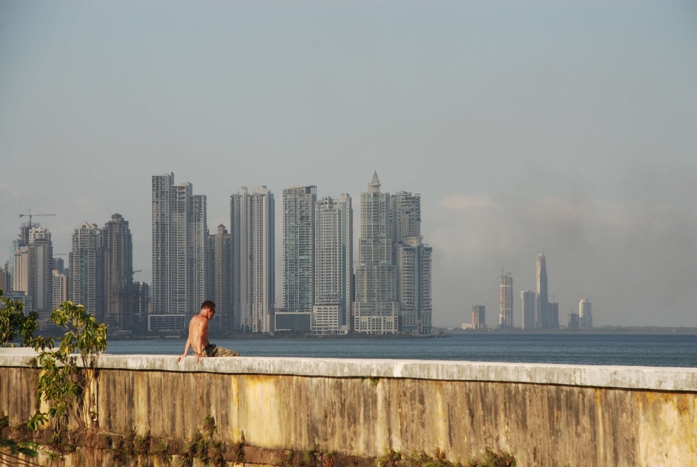 Reflection in Old Panama - young man on a wall with tall buildings in the distance behind him
