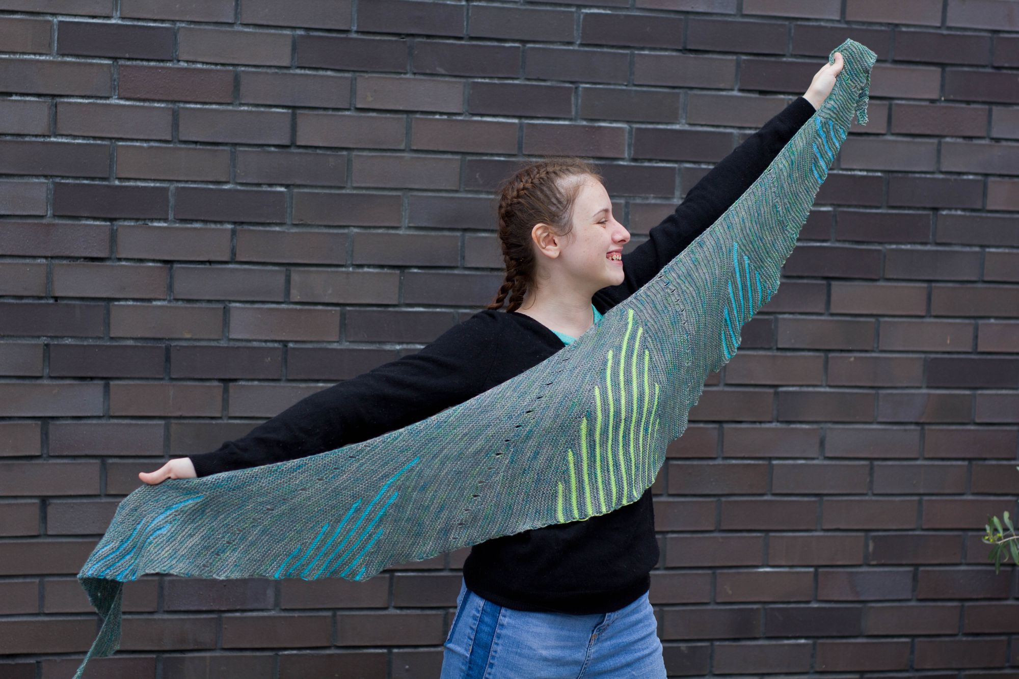 Image of a girl holding a long crescent shaped shawl, with 5 different coloured, different height sections of stripes to look like skylines