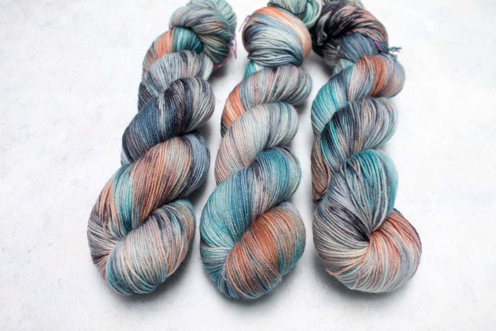 3 skeins of yarn dyed with splashes of orange, teal, blue, black and mushroom