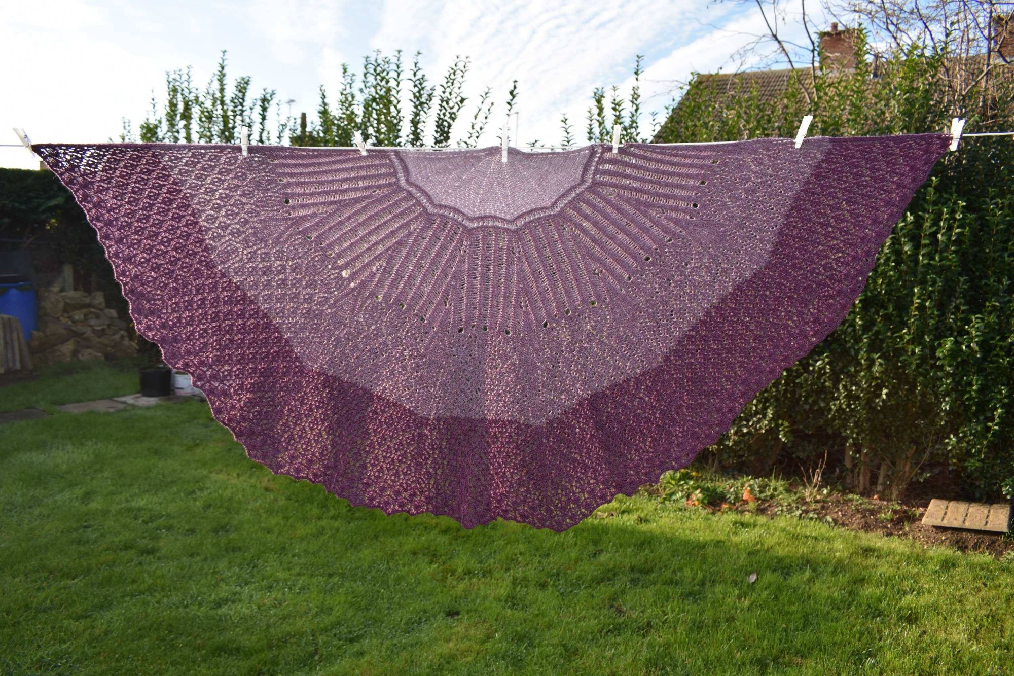 Age of Wonder shawl, hanging on a washing line, spread out, knit in different shades of purple