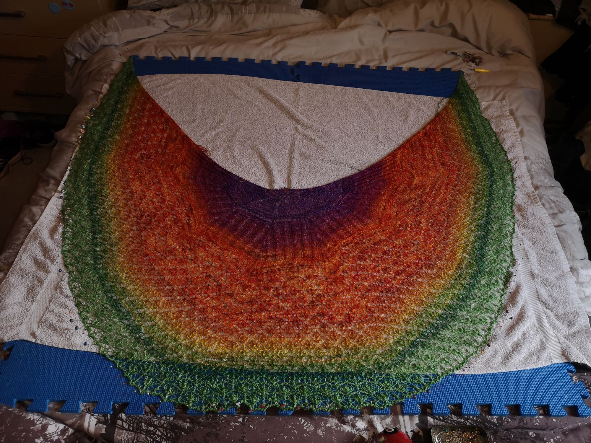 Age of Wonders shawl in a warm, orange to green gradient spread out blocking on a bed