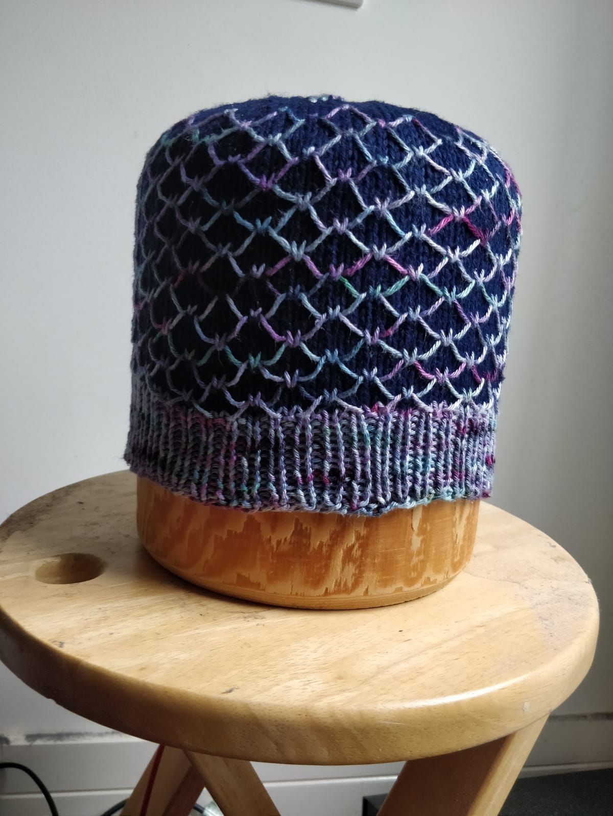 Koah in Dark blue CC and variegated MC on traditional wooden hat blocker on a round wooden table