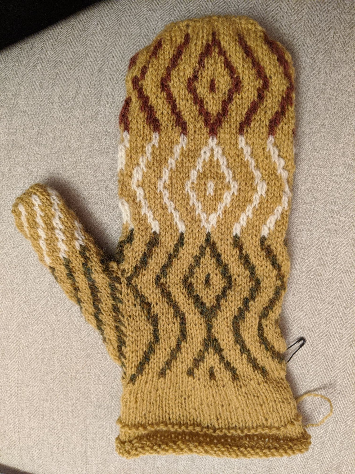 A single left mitt palm side up showing the colourwork road pattern with unfolded hem