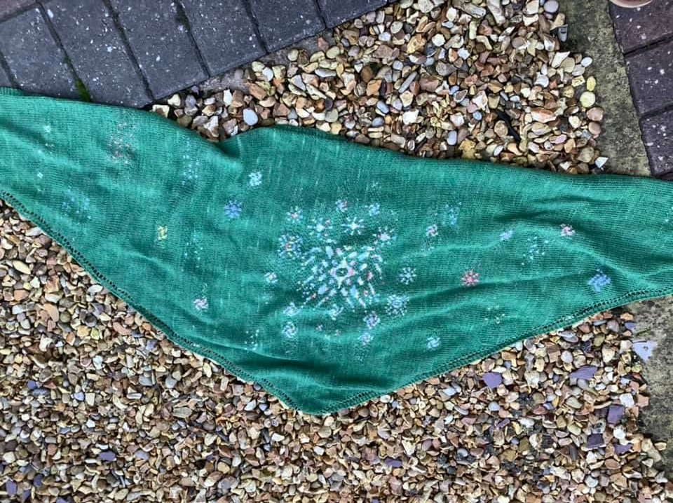 Hanabi shawl in green lying on brown hued gravel