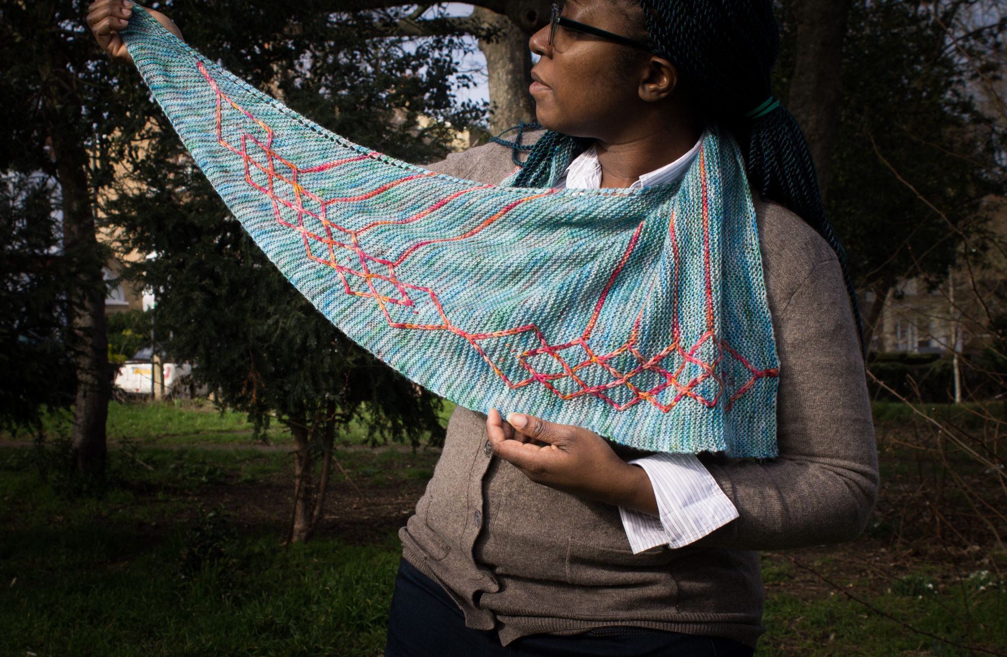 black person holding up blue shawl with a cable pattern in orange running down one edge