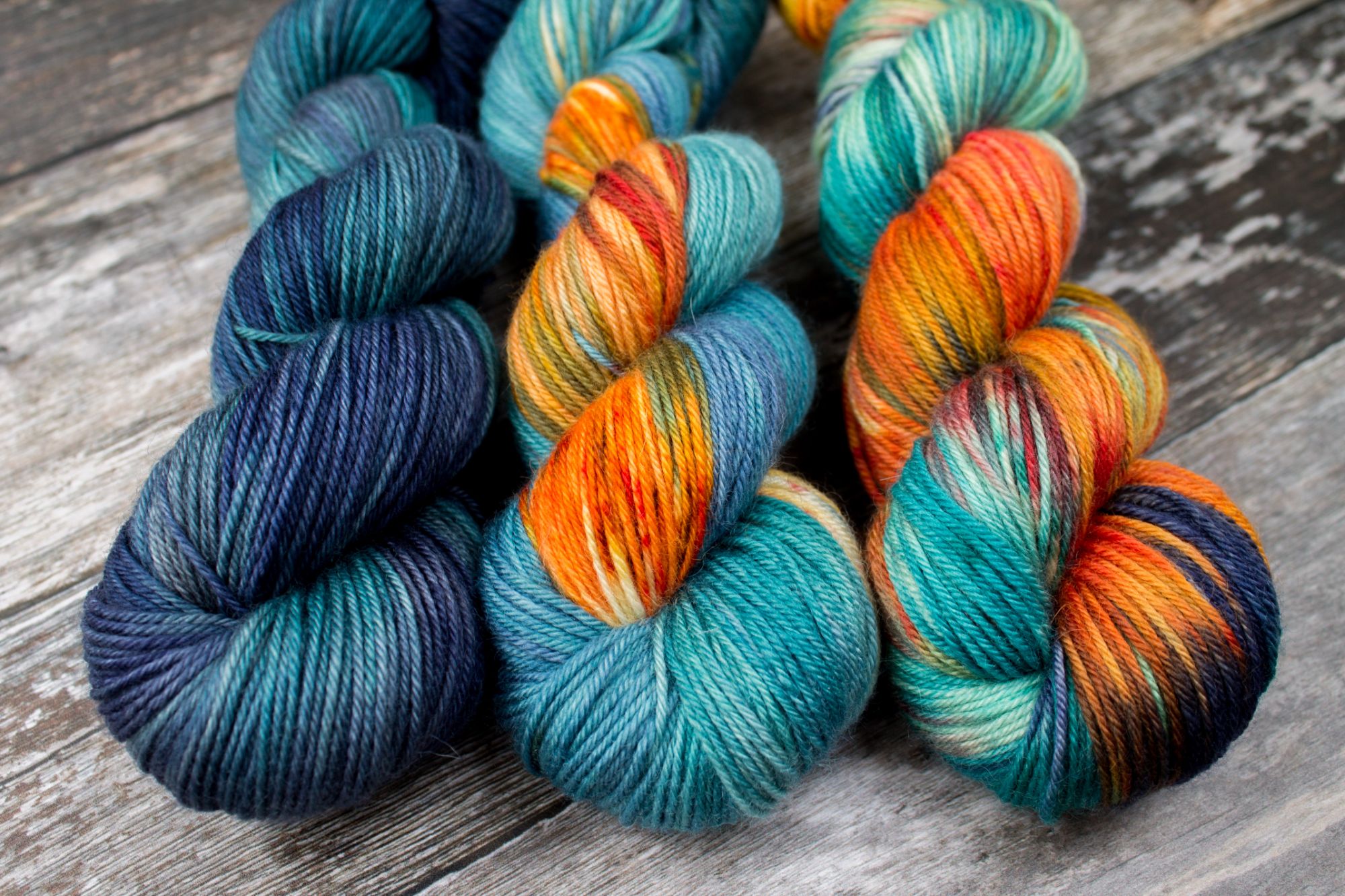 3 skeins, darkest at the black in navy and teal, light navy teal with orange speckled sections, rightmost very variegated teal navy and oranges with gold