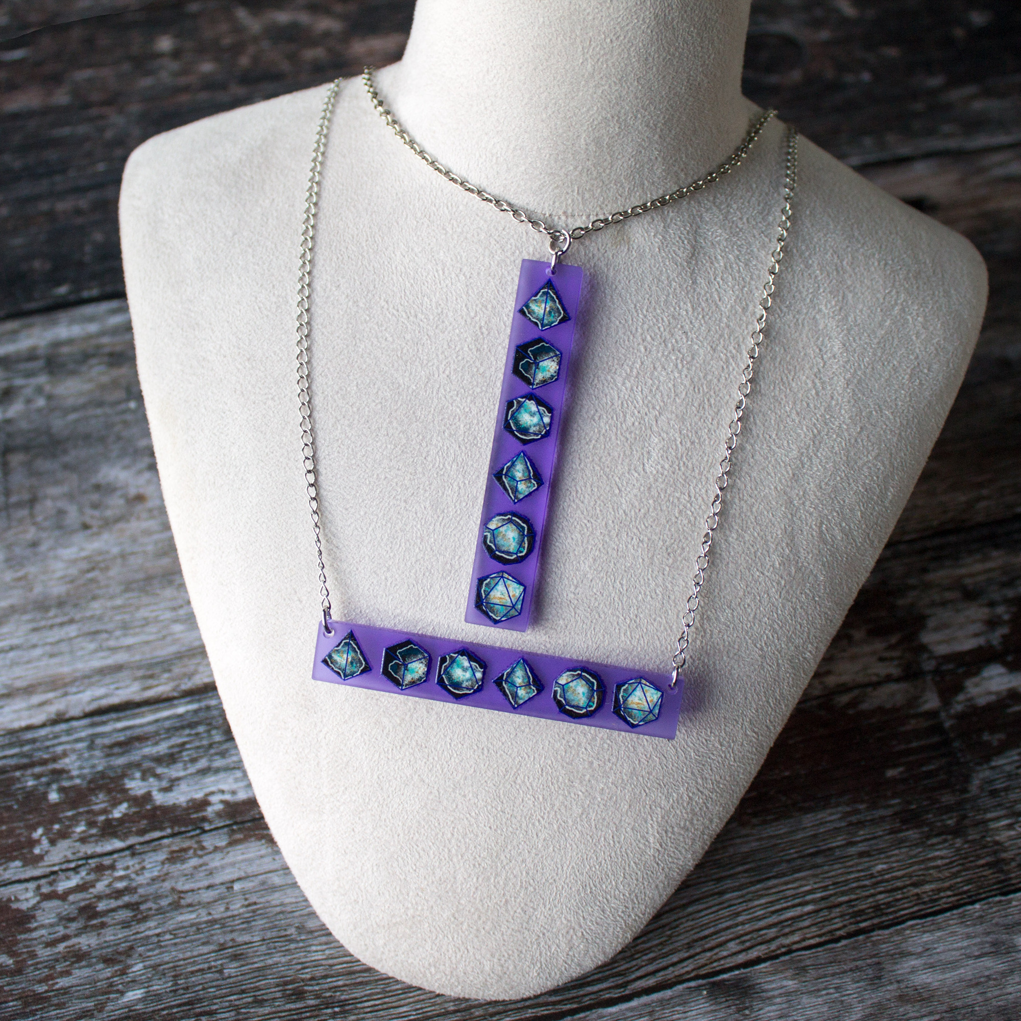 on a display bust are two purple frosted acrylic bar necklaces featuring polyhedral dice designs in a stormy geode.