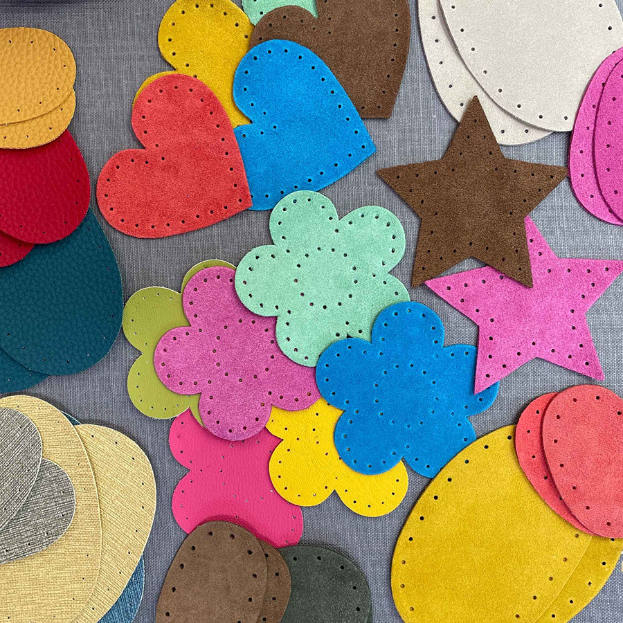 scattered on a surface are several patches in various different shapes in cluding hearts, flowers and stars along with ovals, they all have tiny holes around the edge for sewing on