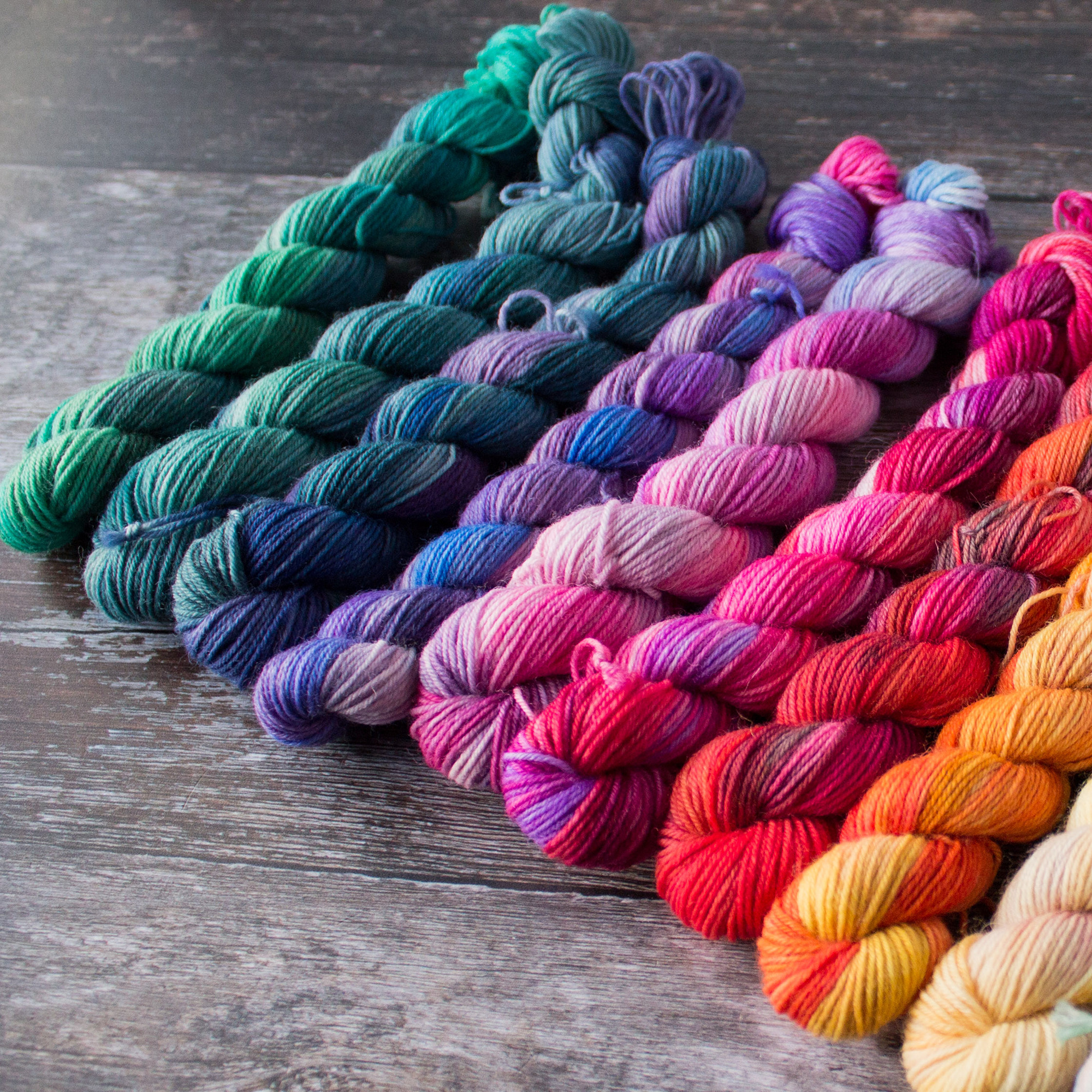 a close up on mini skeins with colourways travelling from red through pin and purple to green teal