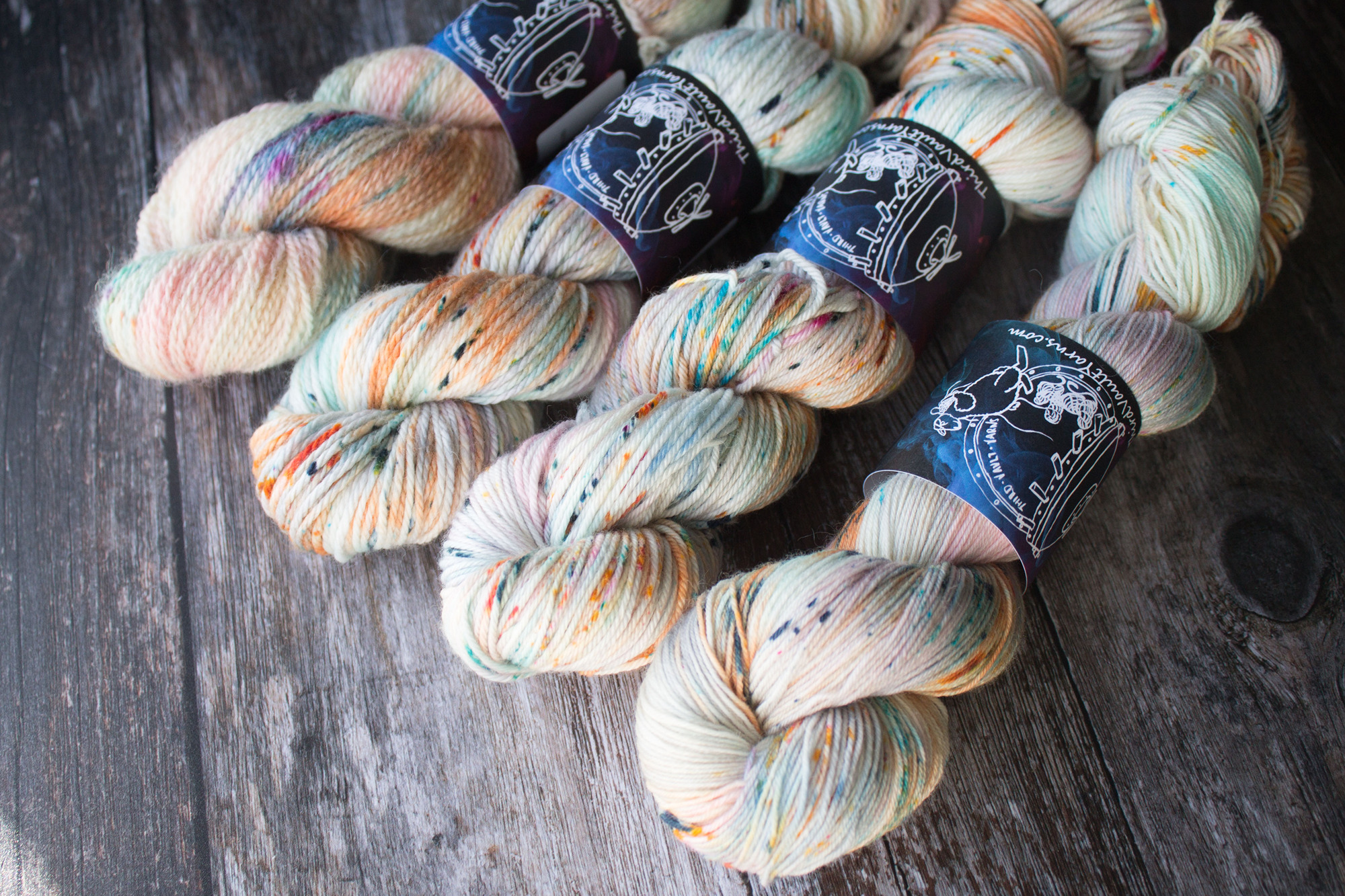 4 skeins fo a cream based yarn with orange blue green and pink speckles laid out on a wood background