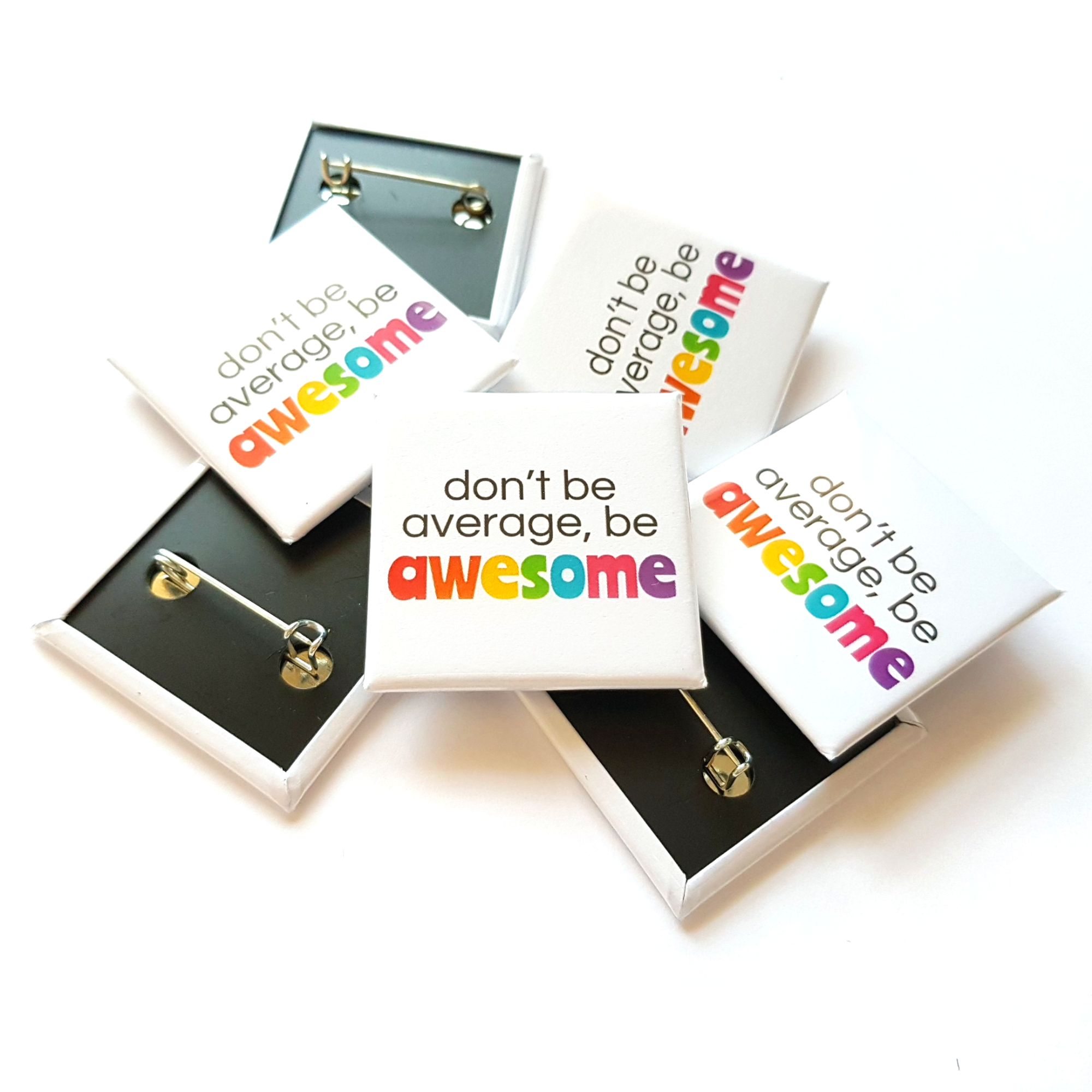 A pile of white square badges with rainbow writing, featuring the phrase 'don't be average, be awesome'