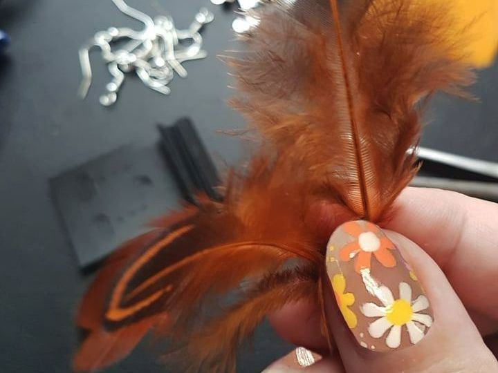 Orange feathers being held between varnished thumb and finger