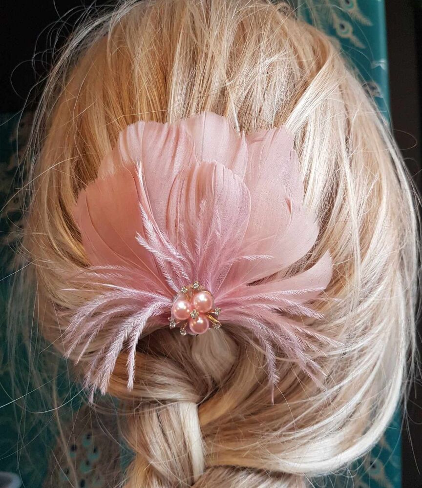 Person wearing a blush pink feather accessory positioned above the ear, sho