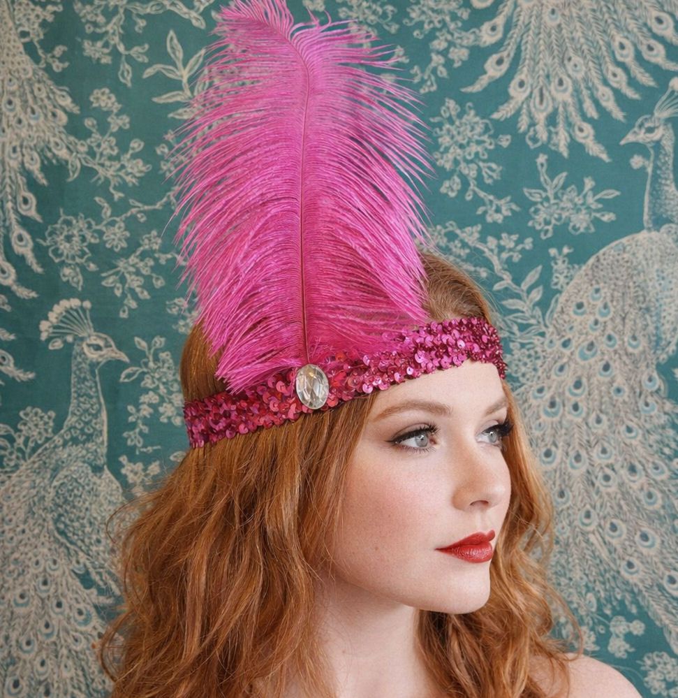 A fair-skinned woman with wavy auburn hair wears a pink sequined headband a