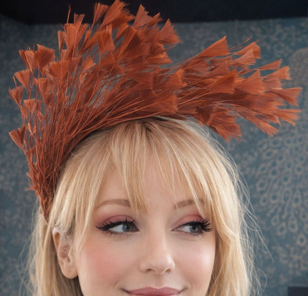 A blonde woman wears a dramatic auburn feather fascinator with jagged, wisp