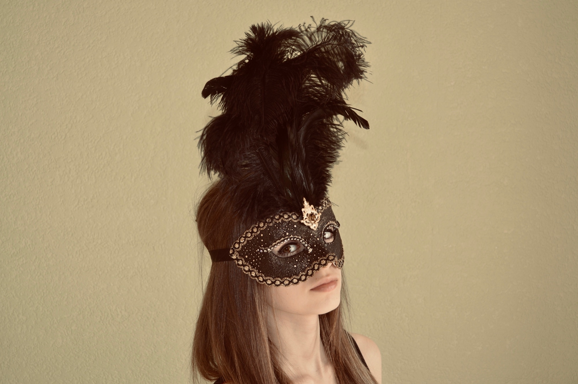 beautiful young girl wearing a black feather mask for her school project and showing what it looks like on