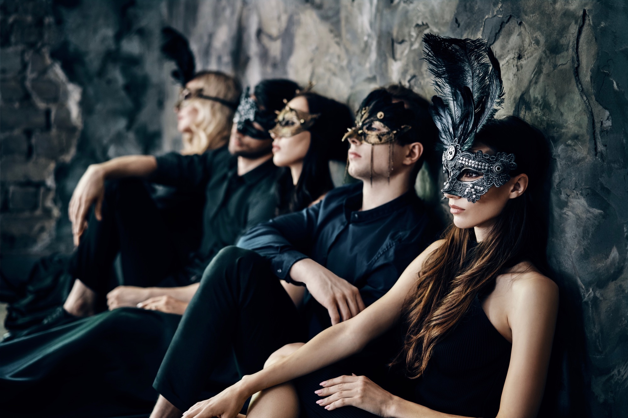 Group of five friends in masquerade masks sitting after a party