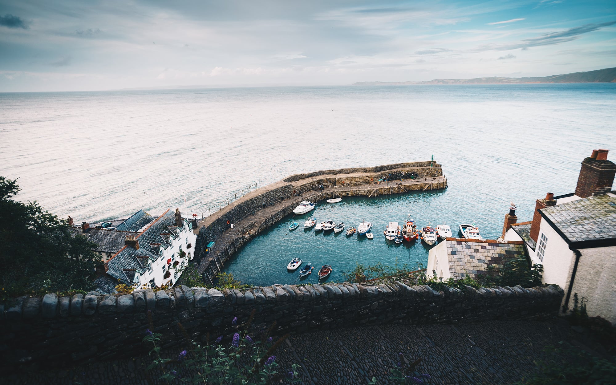 A picture of Clovelly Harbour from higher up in the village, shows the Red Lion Hotel on the left, the harbour wall and few fishing boats on the water