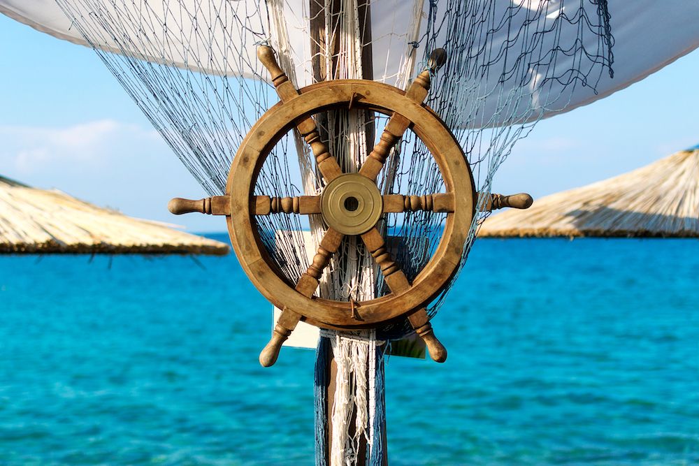 Canva - Wooden ship steering wheel and fishing net on the blue sea and sky