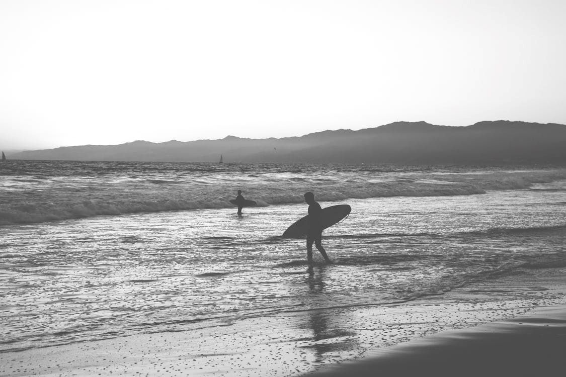 GREY SCALE 2 PEOPLE ON BEACH WITH SURF BOARD