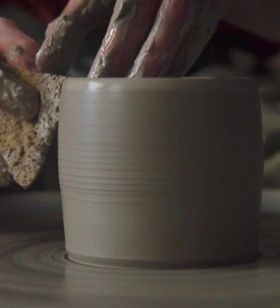 Soft clay form on potters wheel, hands forming shape and holding a sponge